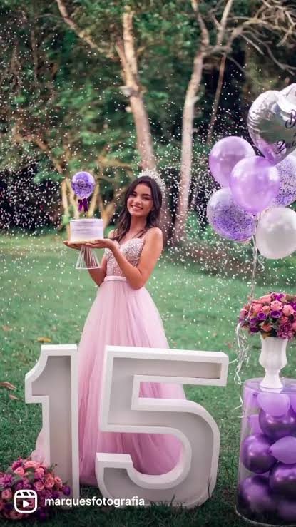 Debutante segurando o bolo no jardim com letras 15 e balões lilás
