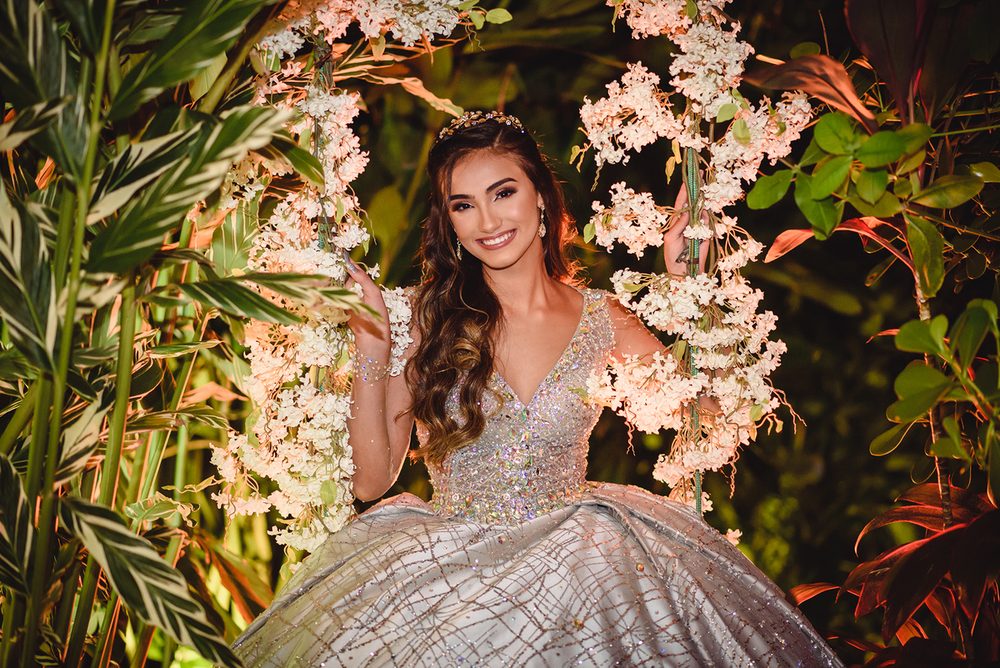 Debutante sorrindo no balanço de flores brancas no jardim