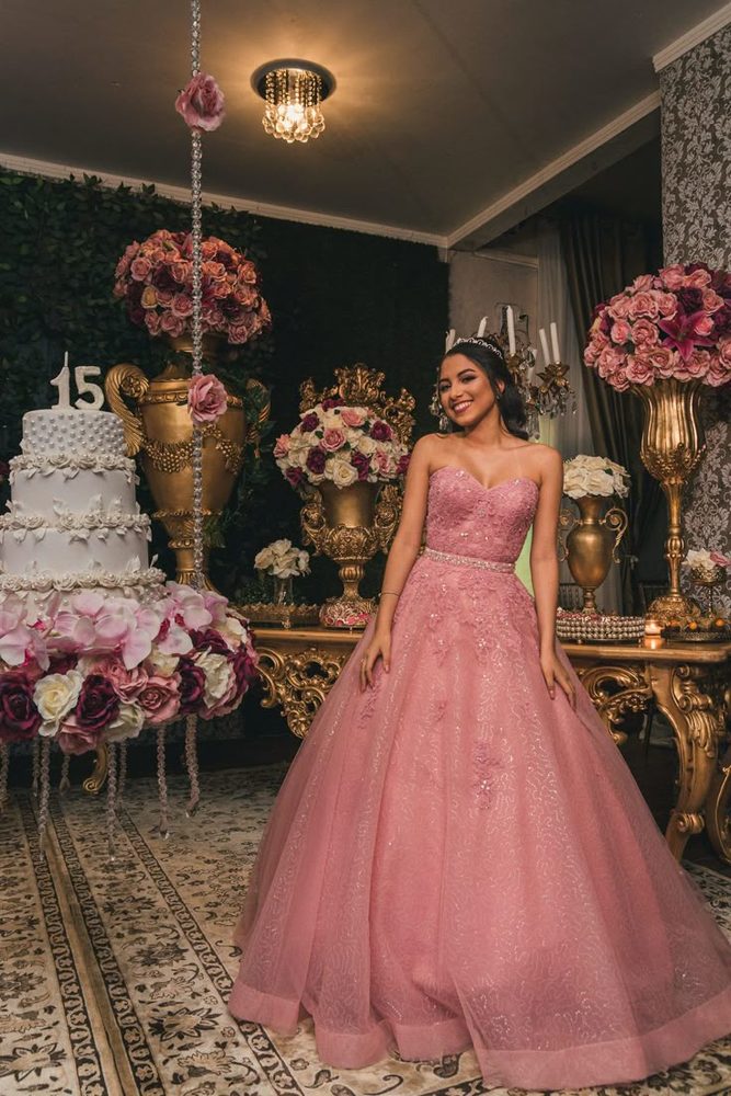 Debutante de vestido rosa ao lado do bolo de 15 anos com vasos dourados