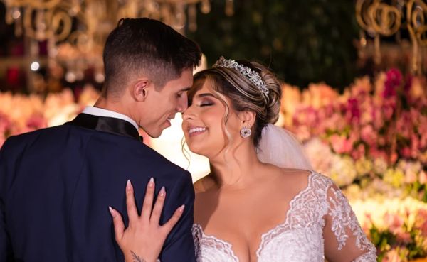 Casal de noivos sorrindo na recepção com flores ao fundo